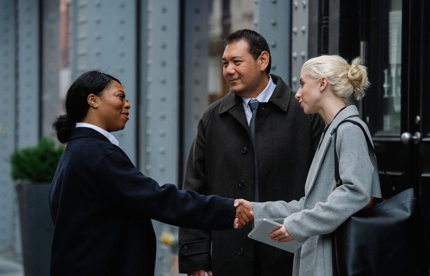 Smiling professionals shake hands during an outdoor business conversation.