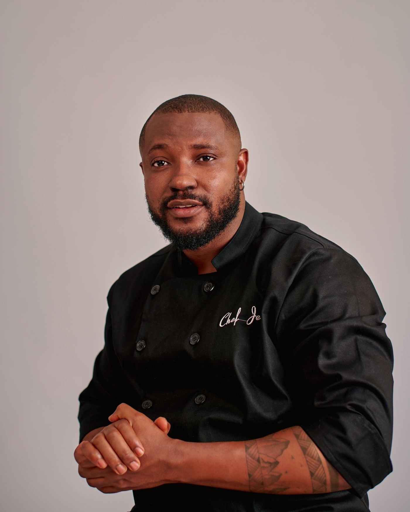 A confident chef poses in a dark chef uniform.