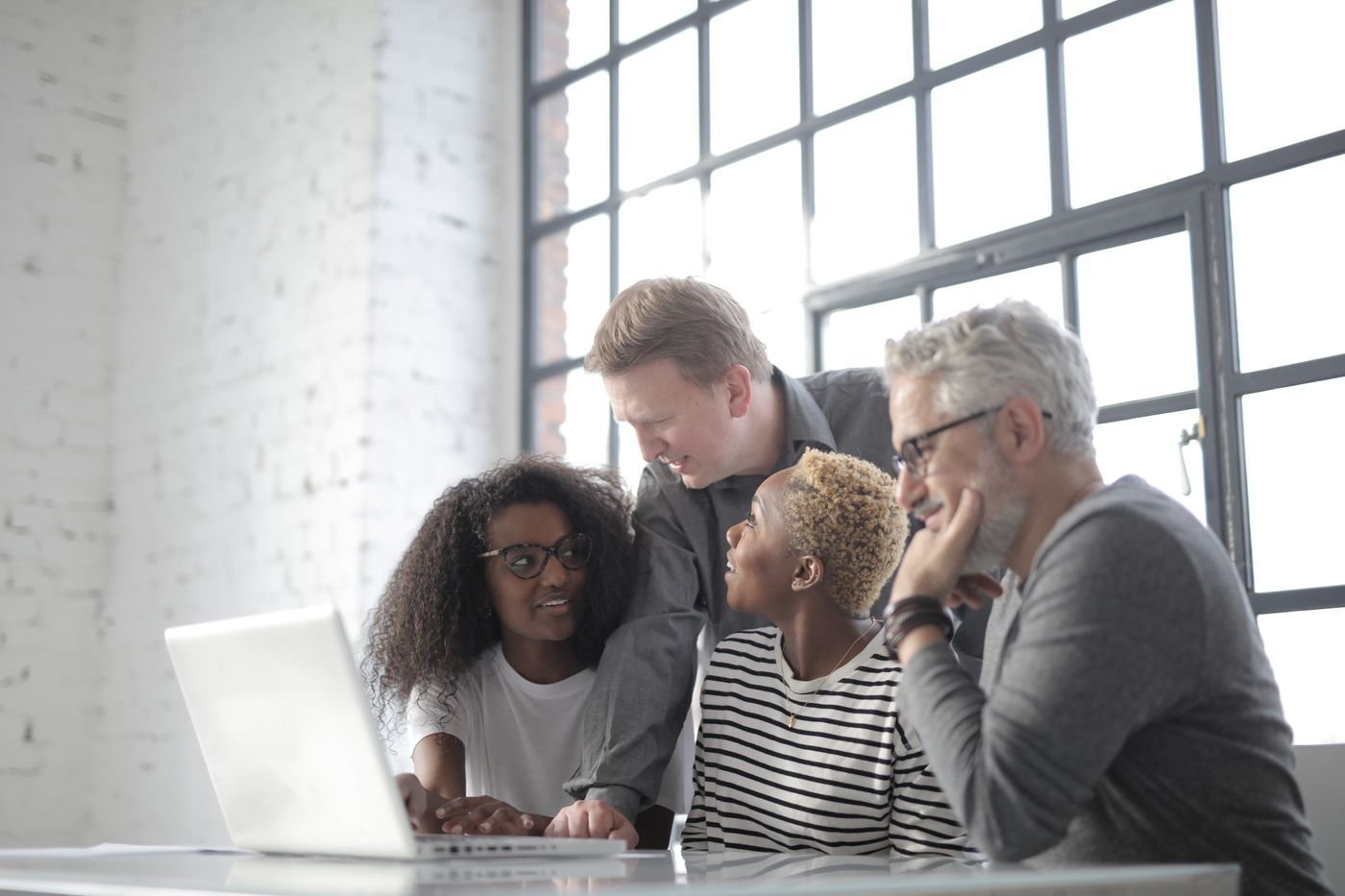 A diverse team collaborates on a laptop in a bright workplace.