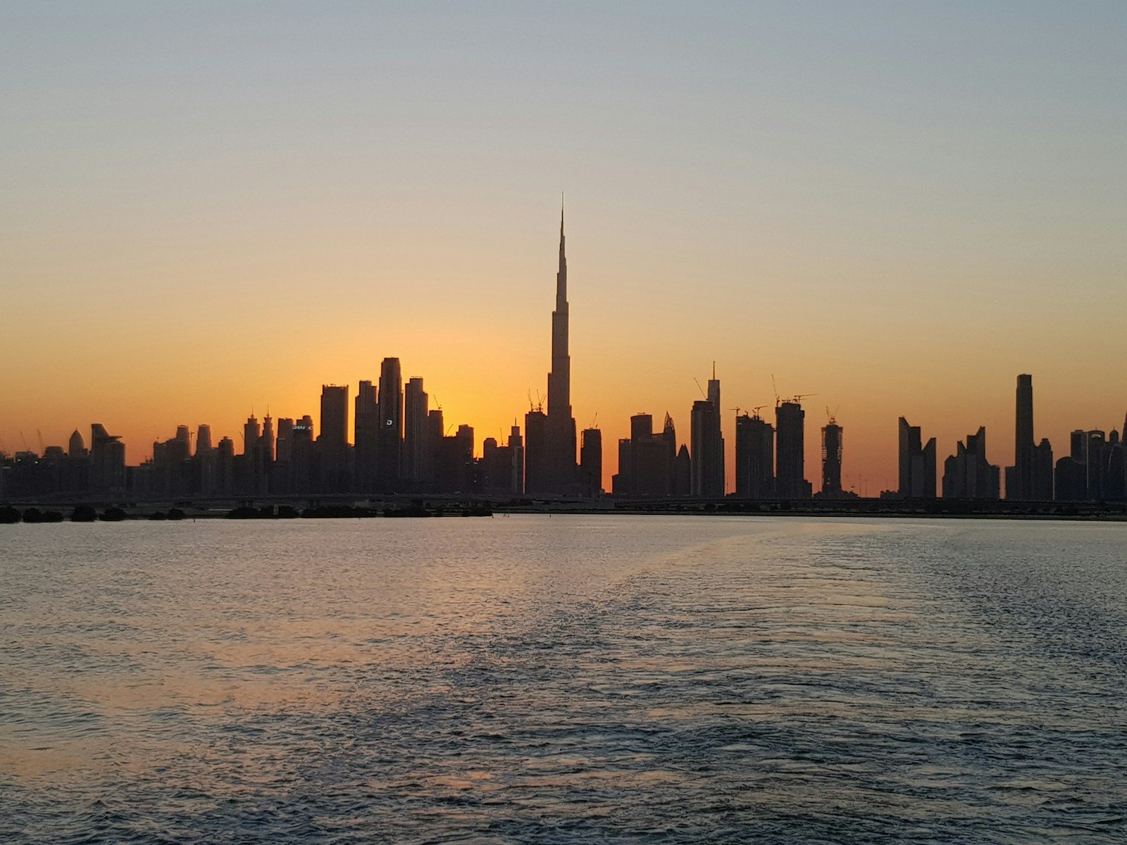 Dubai skyline and Burj Khalifa across water at sunset