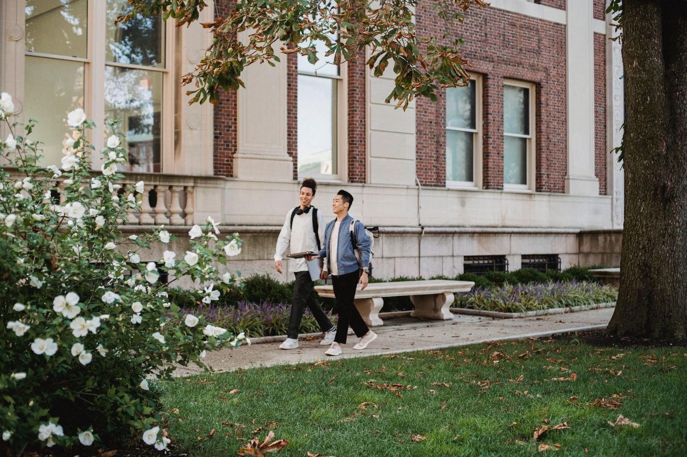 Two smiling students walk and talk along a sunny campus path.