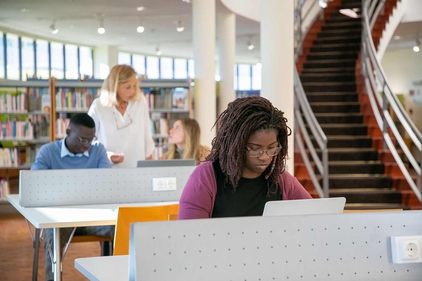 Students work on laptops together in a bright university library.