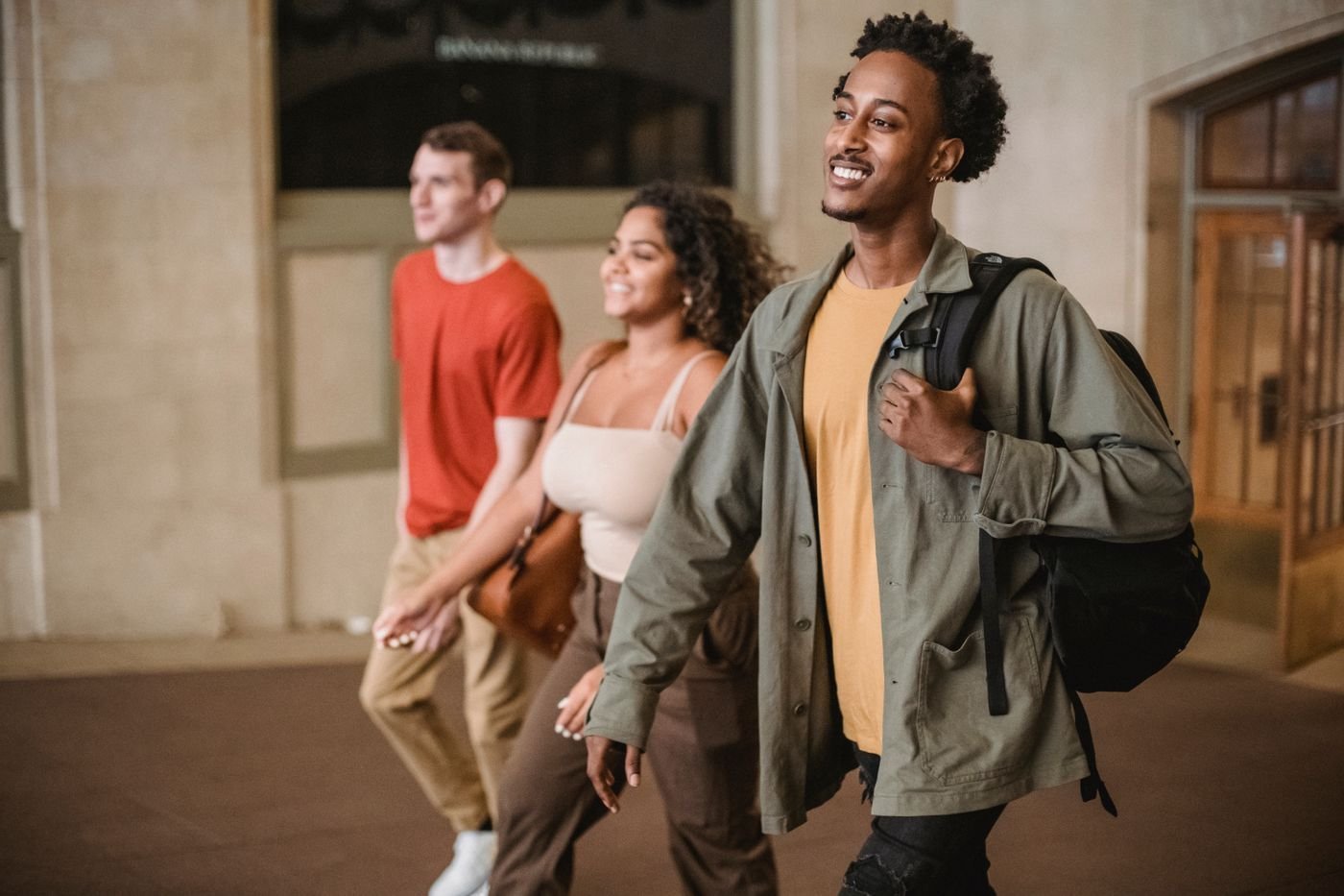 Three students with backpacks walk and chat in a university corridor.