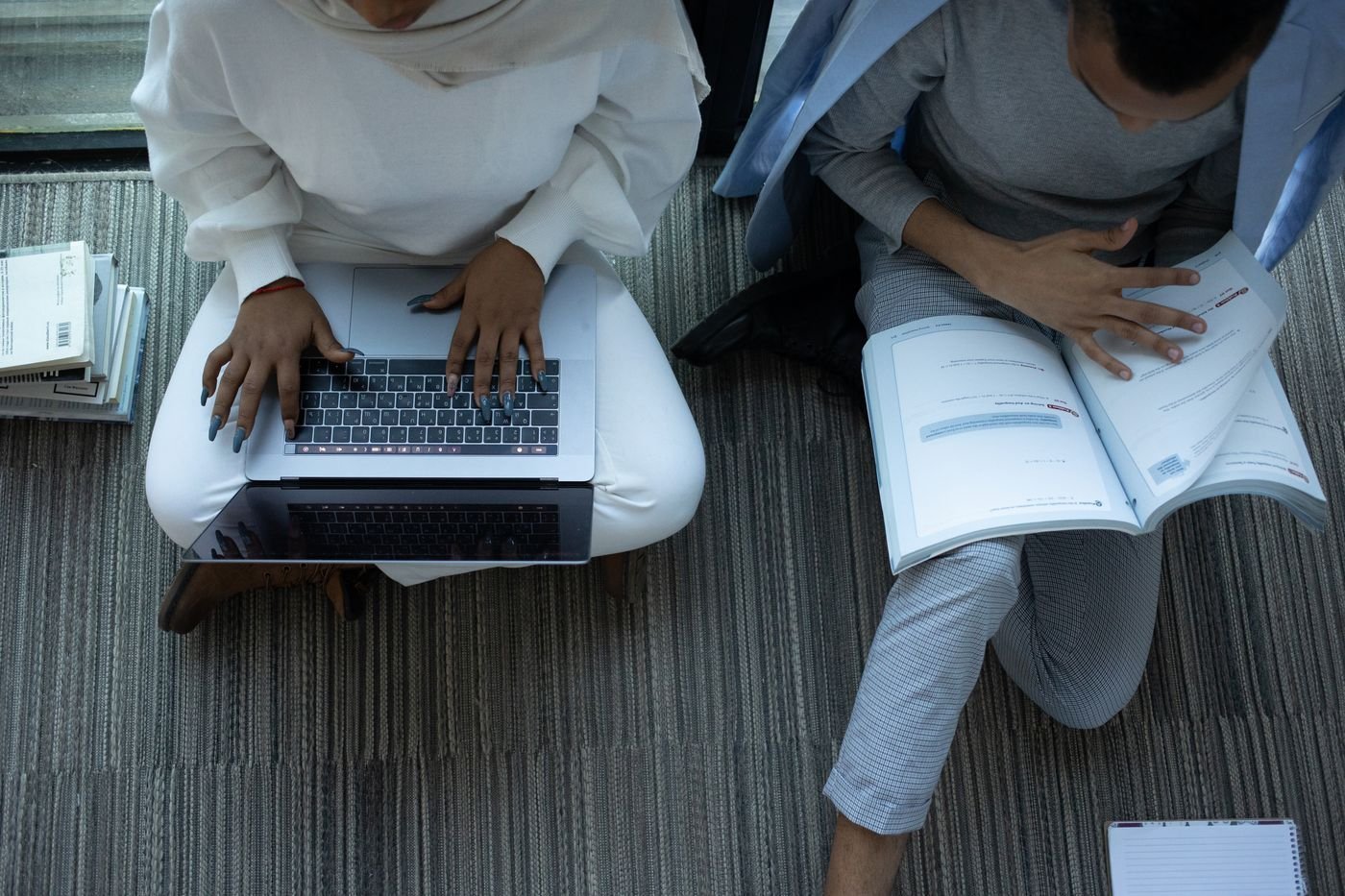 Two students study with a laptop and books at a table.