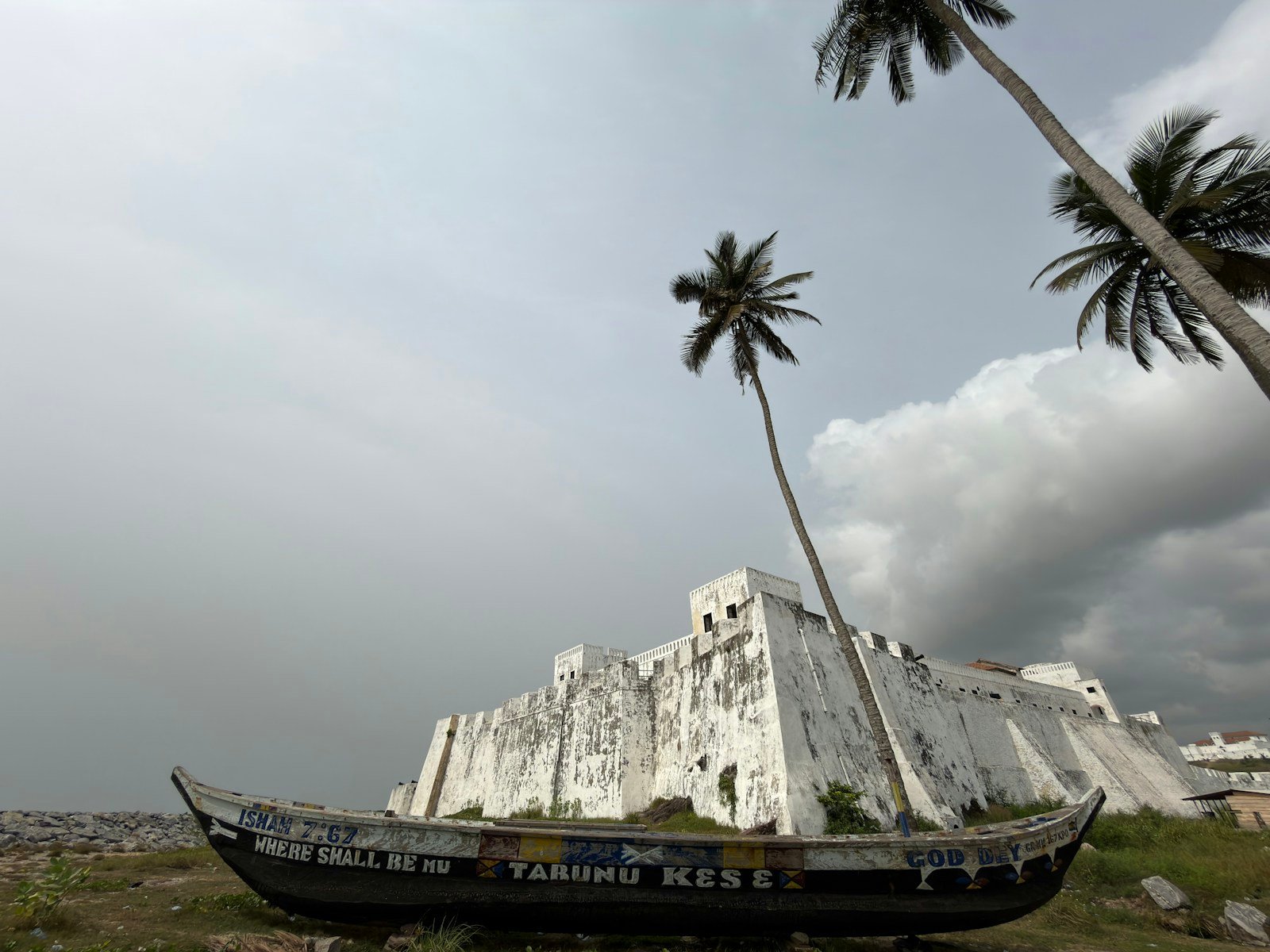 Fishing boat beside historic white Elmina fortress walls