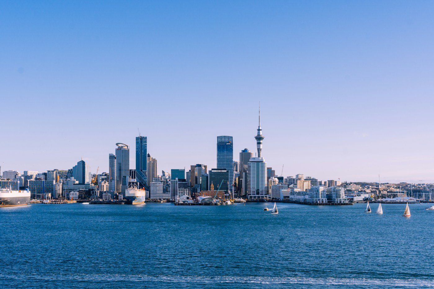 Auckland skyline and Sky Tower across blue harbour water at twilight